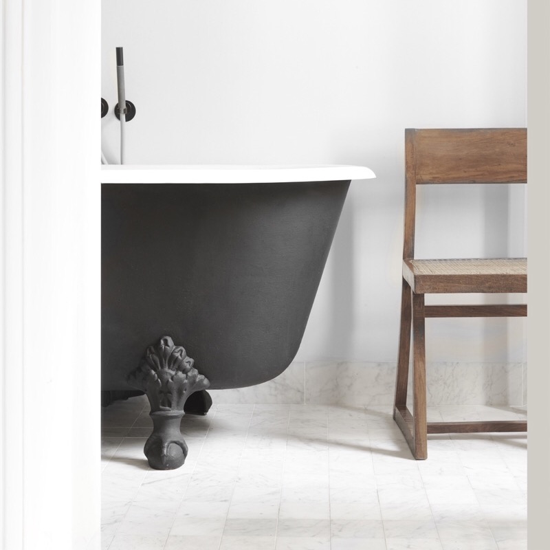 Matt black cast iron bath with a marble tile floor...